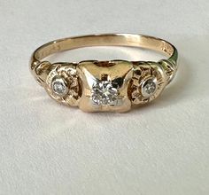 "a most wonderful vintage 14k gold ring with three diamonds, two flowers, and two golds.  this was intended as an engagement ring and likely made in the thirties or forties.  it had one chipped diamond which my jeweler did a beautiful job of replacing and it's looking pretty great for its age.  the central diamond is quite bright and is framed in a bit of white gold, as are the smaller ones.  i LOVE the flower designs around the smaller stones.  ring is marked Fidelity for the maker and 14k with Vintage 14k Gold Three-stone Rings, Vintage 14k Gold Three Stone Rings, Ring With Three Diamonds, Mexican Summer, Random Numbers, Diamond Trilogy Ring, Vintage Gold Engagement Rings, Antique Style Rings, Two Flowers