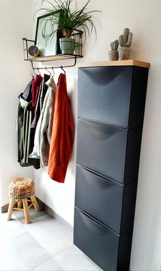 a coat rack with several coats hanging on it next to a stool and potted plant