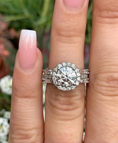 a close up of a person's hand with a ring on their finger and a flower in the background