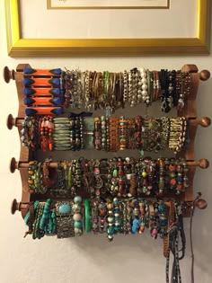 a wooden rack holding bracelets and necklaces in front of a framed picture on the wall