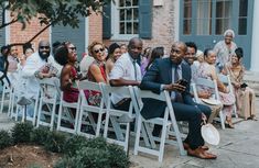 a group of people sitting next to each other on white chairs in front of a building