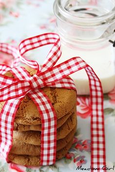 a stack of cookies wrapped in red and white ribbon next to a jar of milk