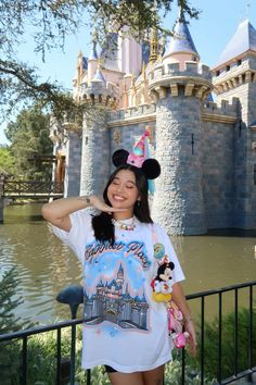 a woman standing in front of a castle wearing a minnie mouse shirt and mickey mouse ears