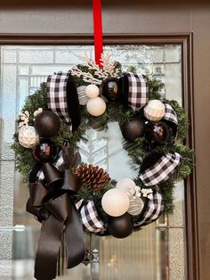 a christmas wreath hanging on the front door with black and white balls, pine cones, and plaid ribbon