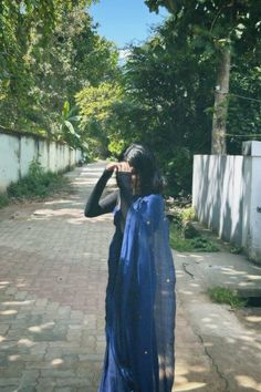 a woman in a blue dress standing on a sidewalk looking through a pair of binoculars