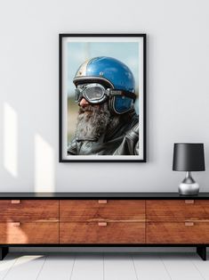 an old man wearing a helmet and goggles is framed in a white wall above a dresser