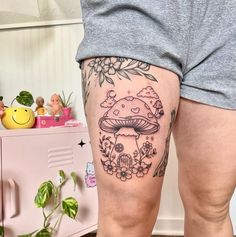 a woman's thigh with a mushroom tattoo on her left leg and flowers in the background