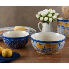 three bowls with yellow and blue designs are on a table next to some lemons