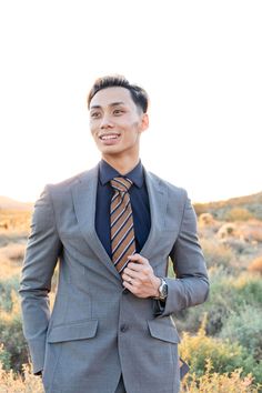 a man wearing a suit and tie standing in the middle of a field with his hands on his hips