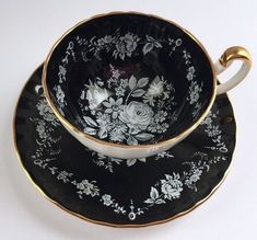 a black and white tea cup with gold trimmings on the side, next to a matching saucer