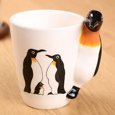 a coffee cup with two penguins on it and one penguin is perched on the mug