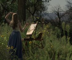 a woman in a blue dress is standing near an easel with a painting on it