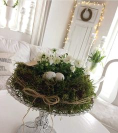 an arrangement of white flowers and eggs in a glass vase on a table with lights