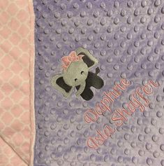 a teddy bear with a pink bow on it's head is sitting on a purple blanket