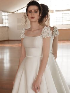 a woman in a white dress standing on a wooden floor with her hands behind her back