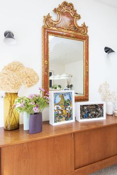 two vases with flowers are sitting on a dresser in front of a mirror that is hanging above it