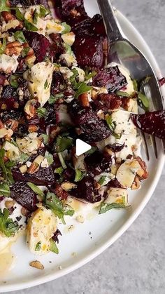 a white plate topped with beets and cheese next to a silver fork on top of a table