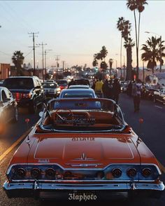 an old car is parked on the side of the road with other cars and people