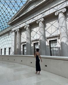 a woman in a black dress is looking up at the skylight inside an indoor building