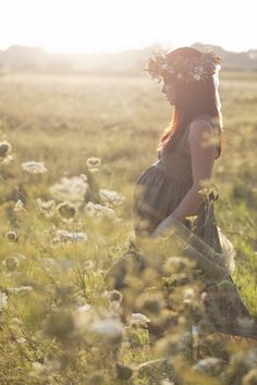 a woman in a field with flowers on her head and sun shining through the grass