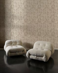 two white chairs sitting next to each other in front of a wall with a pattern on it