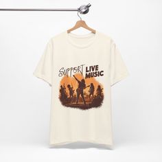 This "Support Live Music" t-shirt is a must-have for any music enthusiast. Ideal for wearing to festivals, live concerts, or casual gatherings, the shirt features a striking design of a guitar silhouette set against a vivid sunset background, symbolizing the passion and vibrancy of live music. Crafted from soft, unisex jersey, this short sleeve tee offers both comfort and style, making it perfect for all-day wear. Its versatile design not only makes a statement but also shows support for musicia Band Logo T-shirt For Music Festivals, Festival Band Merch T-shirt With Logo, Festival Band Logo T-shirt, Band Merch T-shirt For Festival, Band Logo Cotton T-shirt For Festival, Letter Print T-shirt For Music Festival, Summer Band Merch T-shirt, Cotton T-shirt With Band Logo For Festival, Graphic T-shirt For Summer Concerts