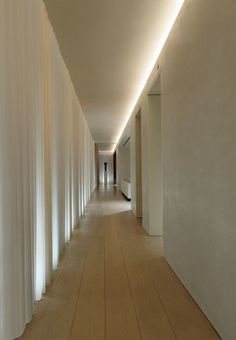 a long hallway with white walls and wooden floors is lit by light from the ceiling