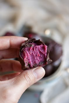 a hand holding a half eaten chocolate covered in raspberry frosting on top of a plate