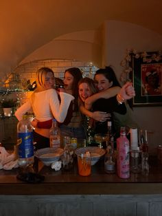 three women are hugging in front of a counter with alcohol bottles and glasses on it