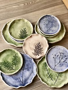 four plates with plants painted on them sitting on a wooden table next to each other