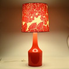 an orange lamp with a red flowered shade on the base and a white wall behind it