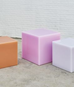 three different colored cubes sitting next to each other in front of a white brick wall