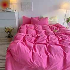 a bed with pink sheets and pillows in a room next to a potted plant