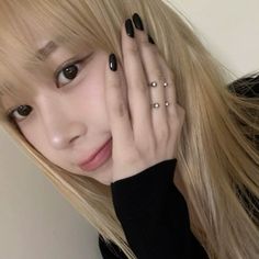 a woman with long blonde hair and black nails holding her hand up to her face