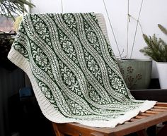 a green and white blanket sitting on top of a wooden chair next to a potted plant