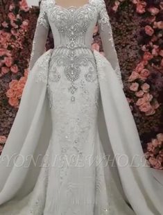 a white wedding gown with long sleeves and a cape on the shoulders, in front of pink flowers