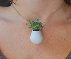 a woman wearing a necklace with a small plant in the vase on it's neck