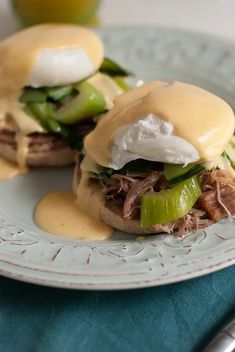 two sandwiches with pickles, cheese and sauce on a plate next to a fork