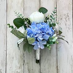 a bouquet of blue and white flowers sitting on top of a wooden table next to a wall