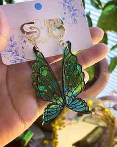 a hand holding a green butterfly shaped earrings