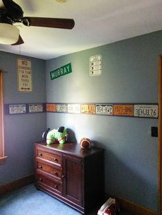 a bedroom with blue carpet and wooden dresser in it's corner, along with several signs on the wall