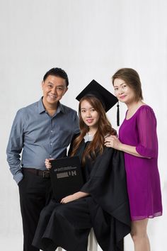 two women and a man posing for a photo with their graduation gowns in front of a white background