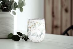 a white vase sitting on top of a wooden table next to a green leafy plant