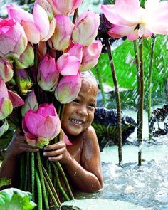 a young boy is holding pink flowers in the water