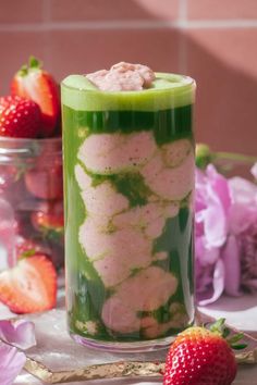 a green drink with strawberries on the side and flowers in the back ground next to it