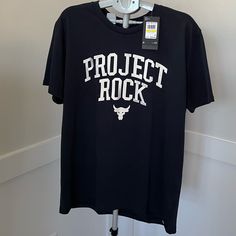 Under Armour Project Rock Shirt Size M New With Tags Under Armour Graphic Print Tops For Streetwear, Under Armour Casual Graphic T-shirt, Under Armour Casual Graphic Print T-shirt, Casual Under Armour Graphic T-shirt, Black Rock Crew Neck Shirt, Black Crew Neck Rock Shirt, Casual Under Armour Tops With Logo Print, Under Armour Black Tops With Letter Print, Black Under Armour Top With Letter Print