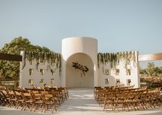 an outdoor ceremony setup with wooden chairs and greenery on the walls, in front of a circular archway