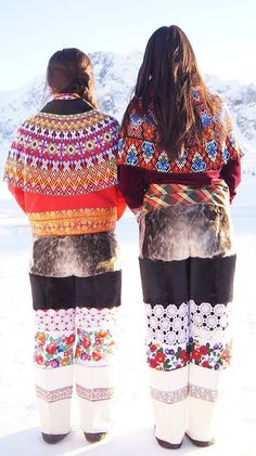 two women standing in the snow with their backs to each other, wearing colorful clothing