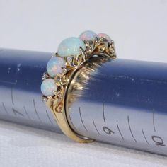 "This Victorian ring was handcrafted in England around 1900. It's a glimmery little stunner featuring five round cabochon opals patterned with 10 rose cut diamonds. The largest opal can be found at the center of the ring face, it measures 5.3 mm in diameter and 3.3 mm in depth. This piece is a size 8.25 and it weighs 4.5 grams. The ring face measures 7.5 x 22.5 and it sits 5.4 mm off the finger. It bears the gold purity mark, \"18 C\". Opals look like the universe and all her colors inside one t Heirloom Multi-stone Diamond Opal Ring, Heirloom Multi-stone Opal Diamond Ring, Opal Jewelry With Rose Cut Diamonds, Round Opal Jewelry With Rose Cut Diamonds, Diamond Multi-stone Opal Ring, Victorian Yellow Gold Opal Jewelry, Victorian Opal Yellow Gold Jewelry, Victorian Opal Jewelry In Yellow Gold, Victorian Style Opal Round Rings