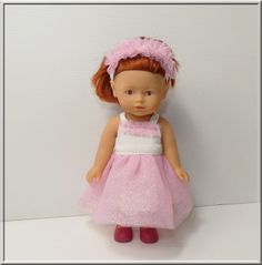 a doll with red hair wearing a pink and white dress, standing in front of a wall